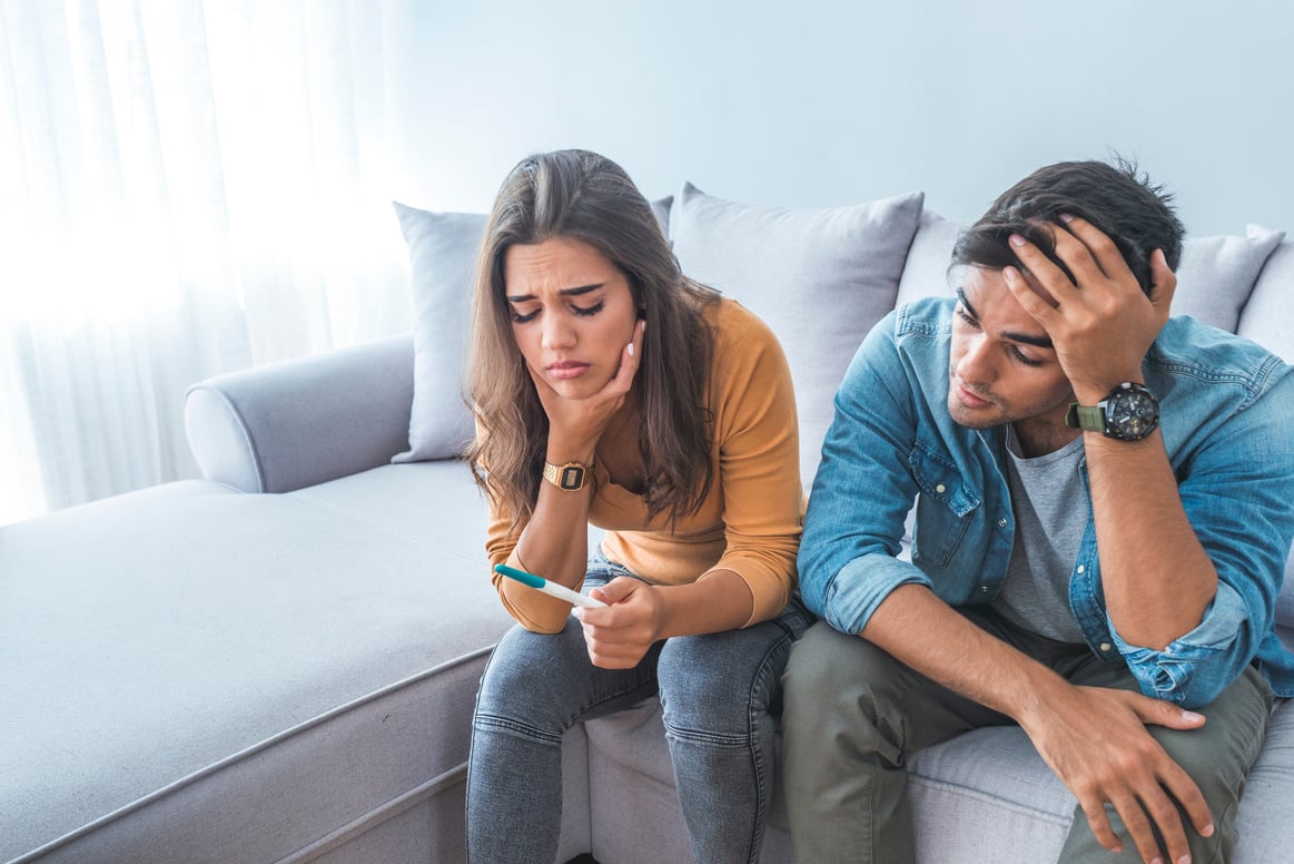 Sad stressed couple with pregnancy test sitting at home