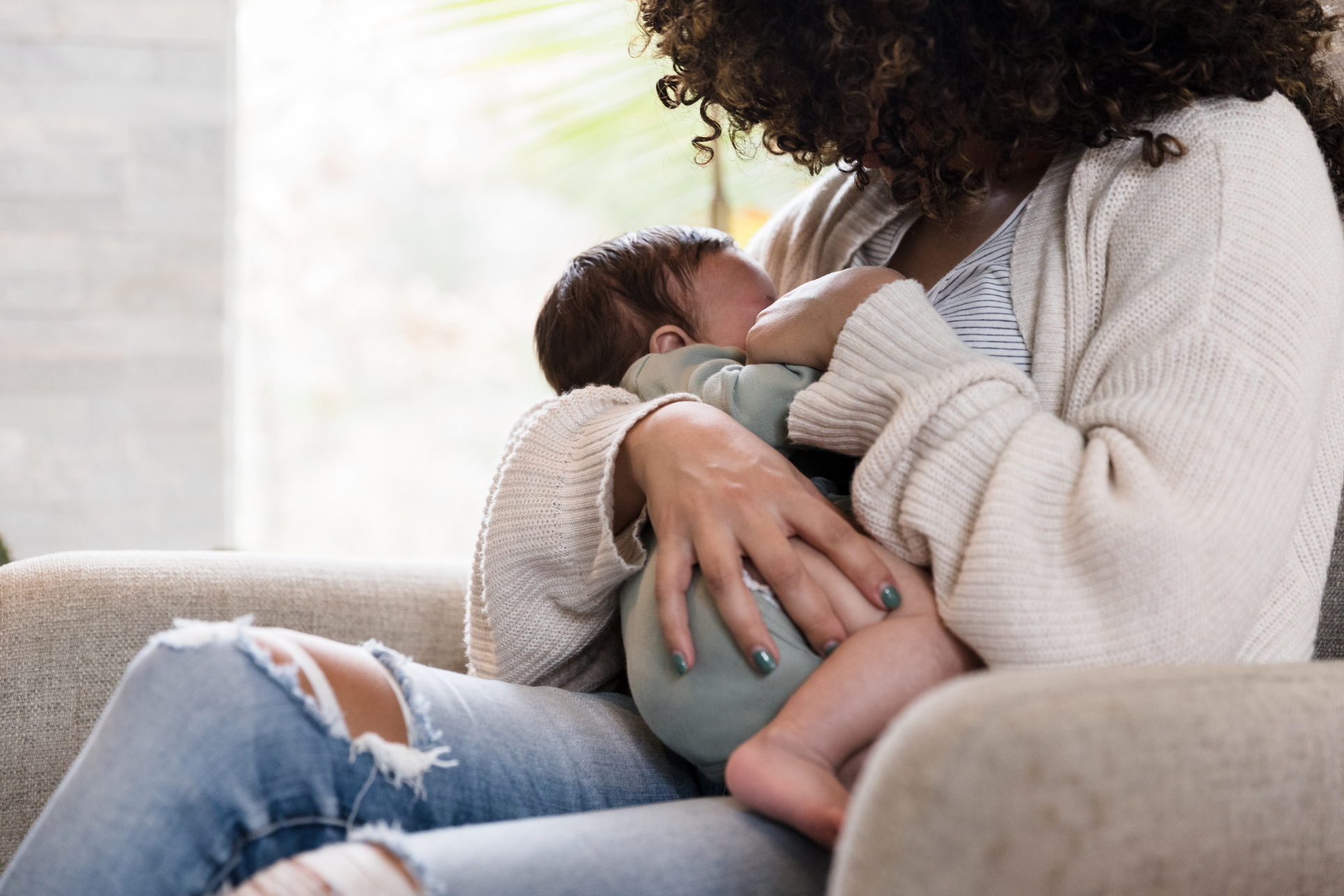 Unrecognizable mom holds baby snugly while breastfeeding