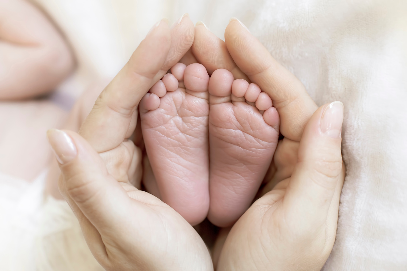 Mom Holds in Her Hands the Feet of Newborn Baby